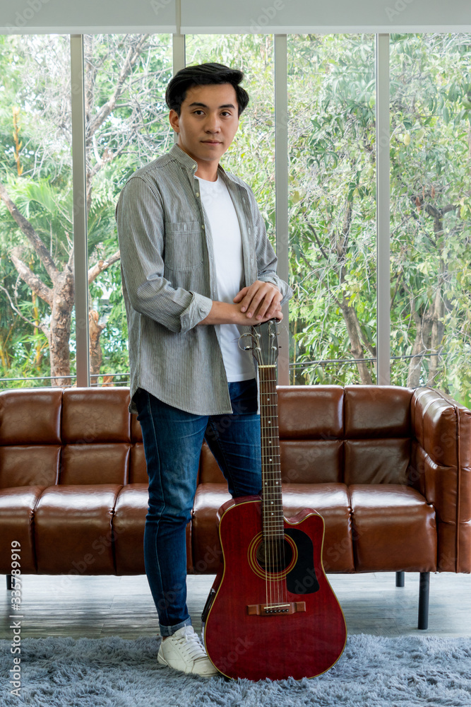 Young guitar player holding his guitar at home. Music and song concept.