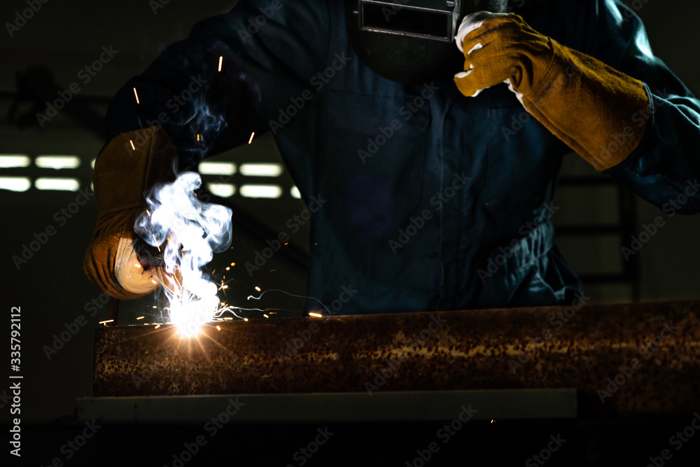 Metal welder working with arc welding machine to weld steel at factory while wearing safety equipmen