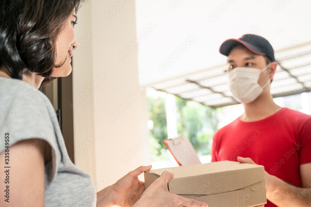 亚洲邮递员或送货员在家门口给年轻的女顾客提小盒快递