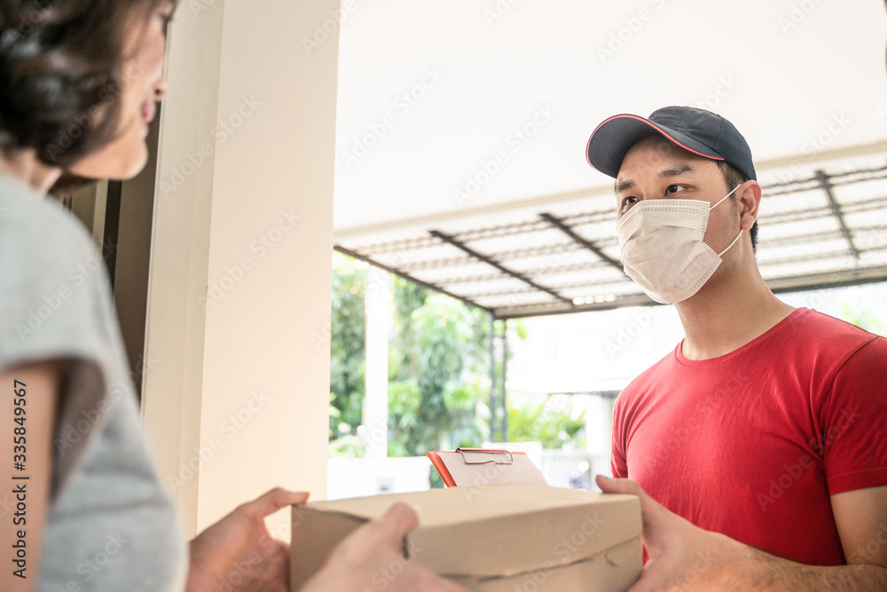 亚洲邮递员或送货员在家门口给年轻的女顾客提小盒快递