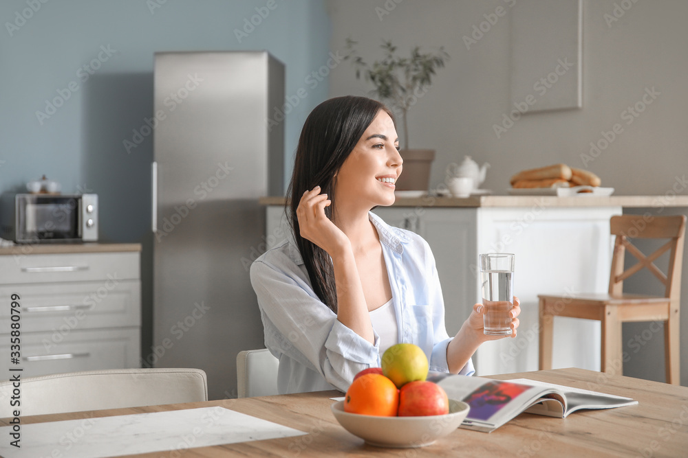 Beautiful young woman drinking water in kitchen