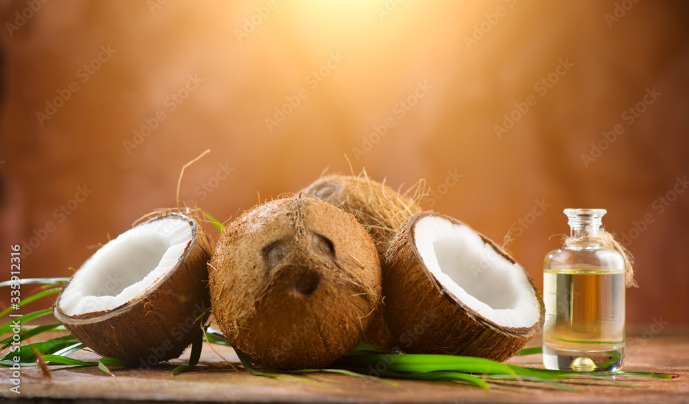 Coconut palm oil in a bottle with coconuts and green palm tree leaf on brown background. Coco nut cl