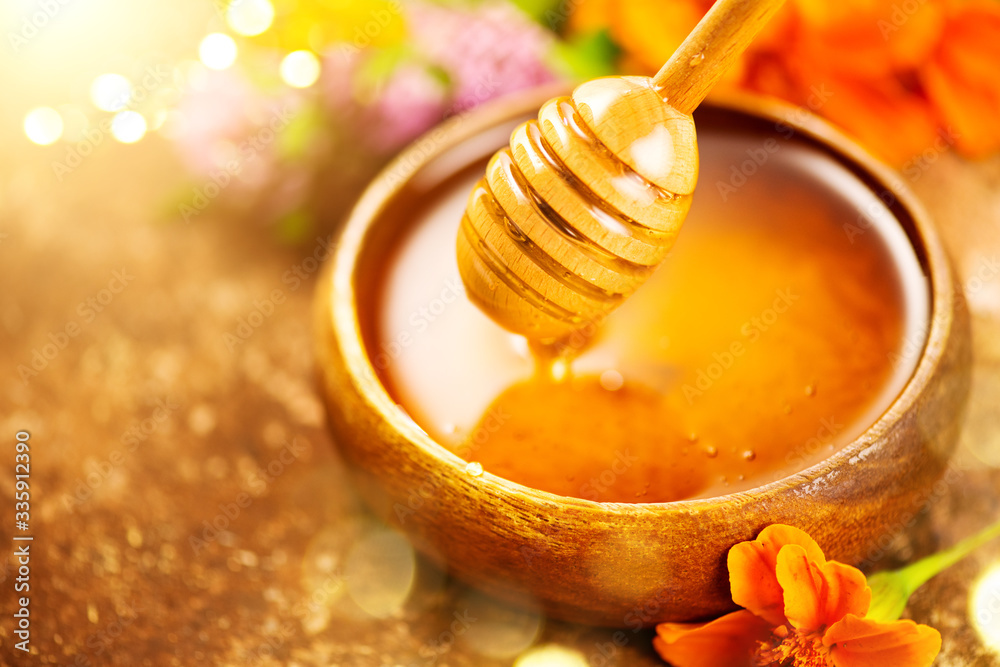 Honey dripping from honey dipper in wooden bowl.  Close-up. Healthy organic Thick honey dipping from