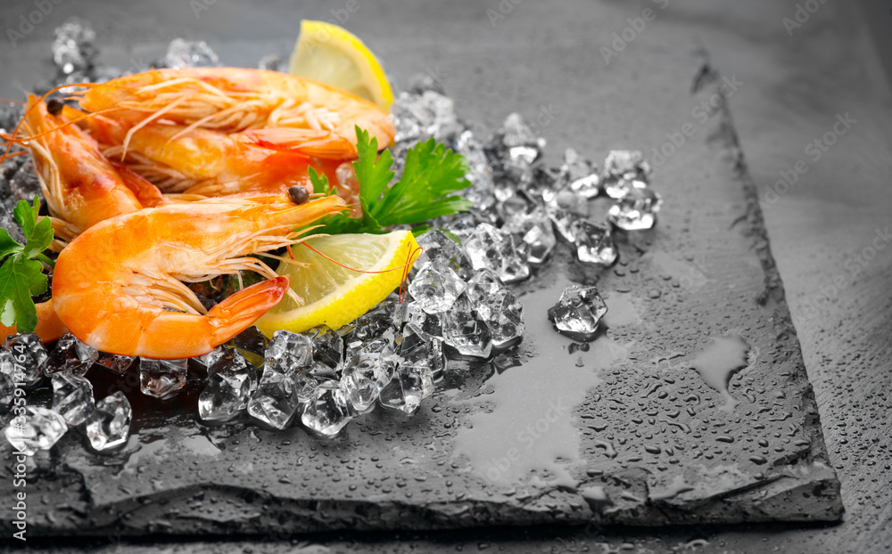 Shrimps. Fresh Prawns on a Black slate Background. Seafood on crashed ice served with herbs, dark ba