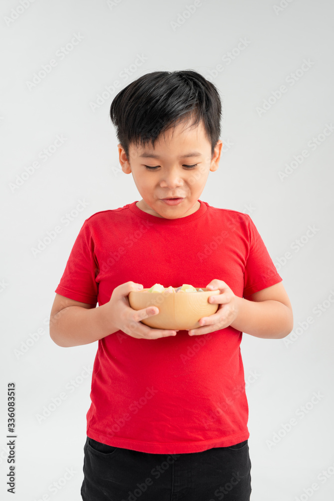 Schoolboy holds a yellow bowl full of candy. Portrait of a child of asian appearance and delicious f