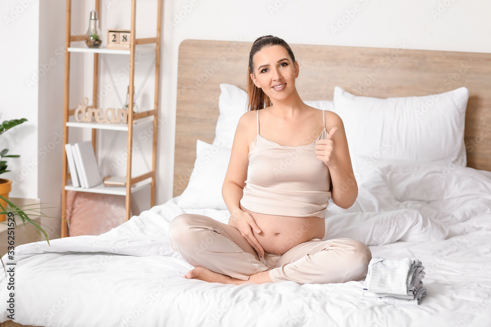 Beautiful pregnant woman showing thumb-up in bedroom