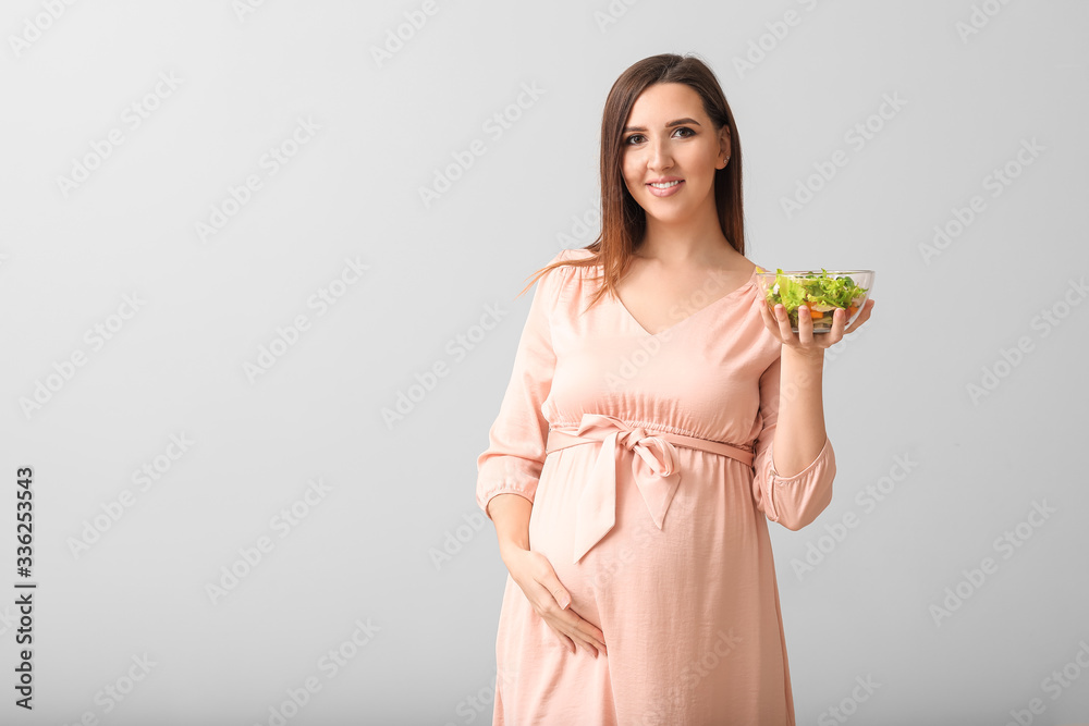 Beautiful pregnant woman with healthy salad on grey background