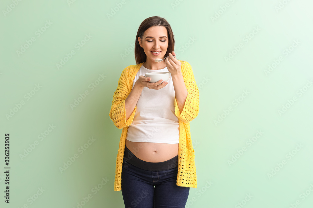 Beautiful pregnant woman with yogurt on color background