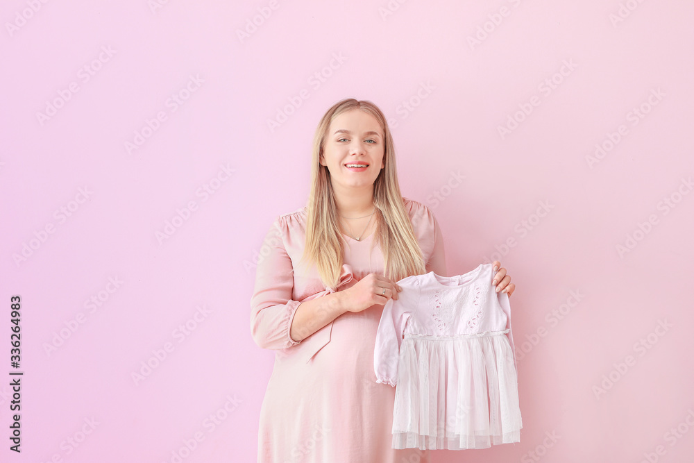 Beautiful pregnant woman with baby clothes on color background