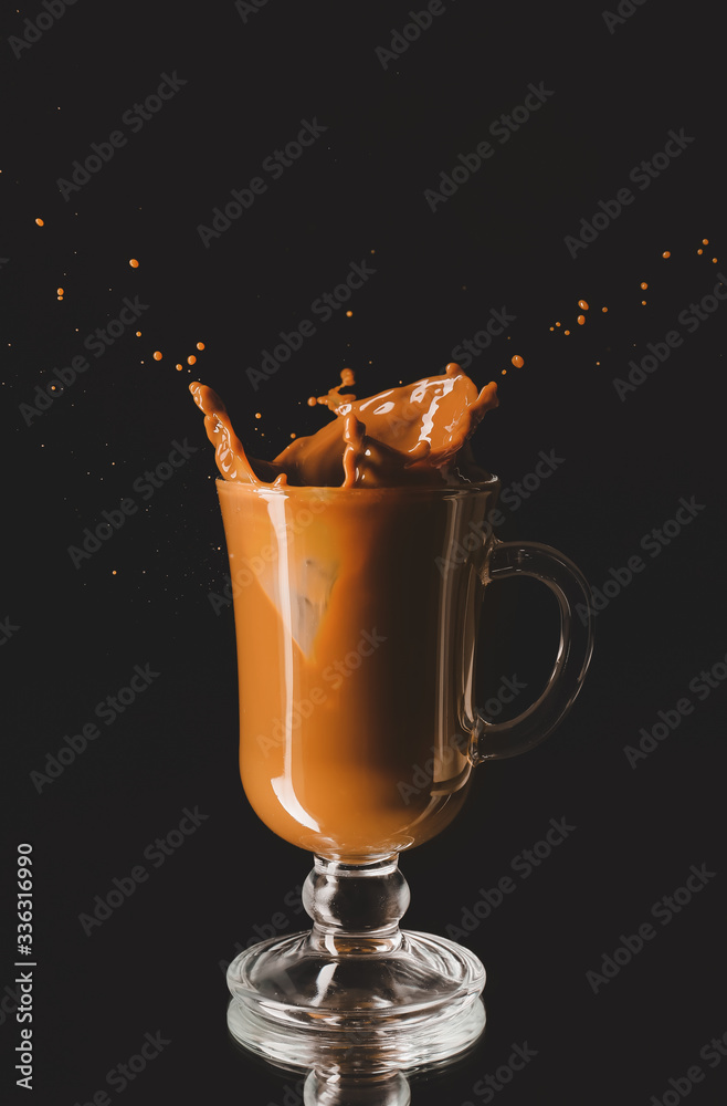 Splashing of coffee in glass cup on dark background