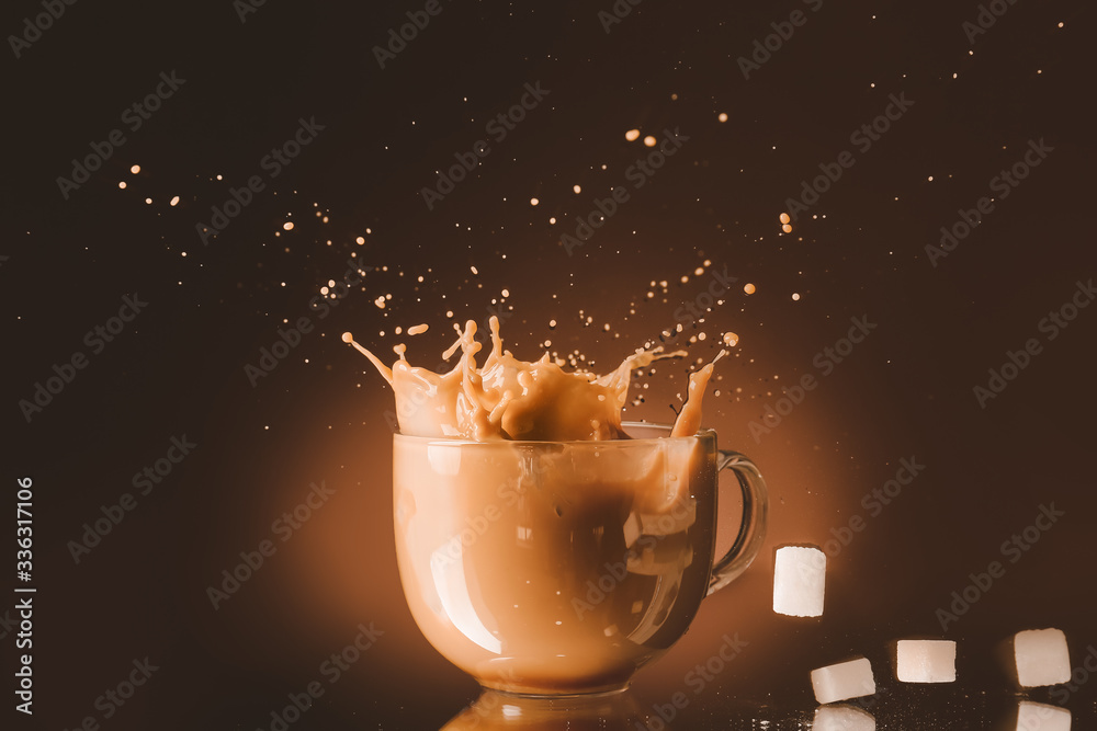 Splashing of coffee in glass cup with sugar on dark background