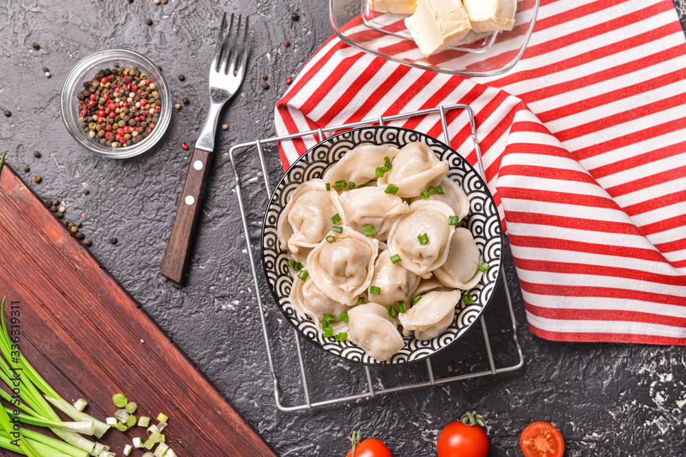 Bowl with tasty dumplings with spices and onion on dark background