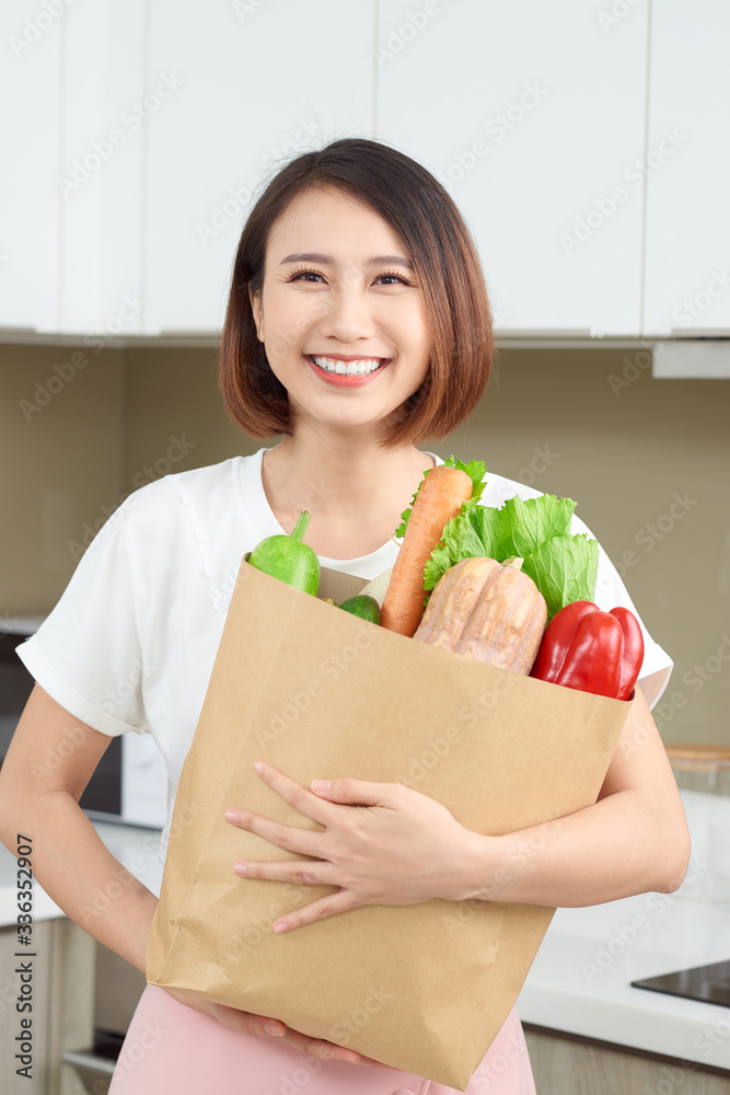 Young Asian woman holding grocery shopping bag with vegetables in the kitchen.