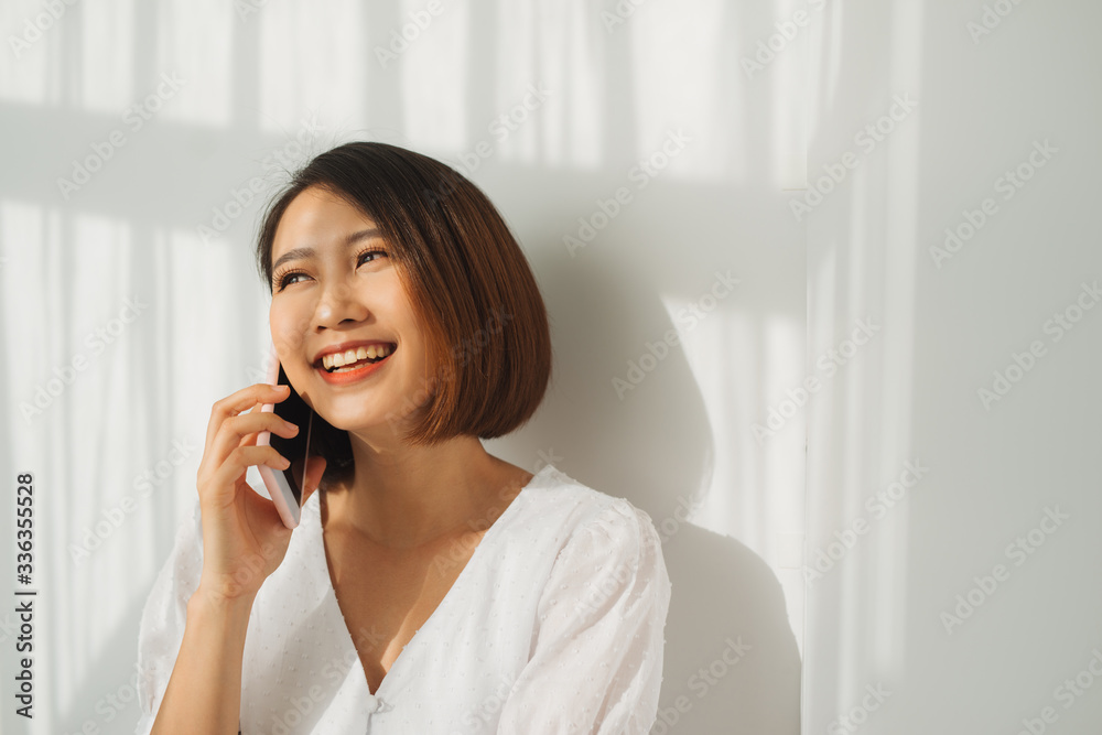 Asian young woman over isolated white wall keeping a conversation with the mobile phone