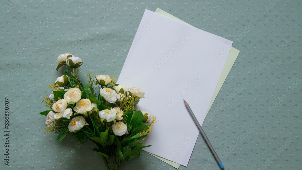 Top view: blue pencil, paper, a bunch of white flowers against green patterned tablecloth. Empty spa