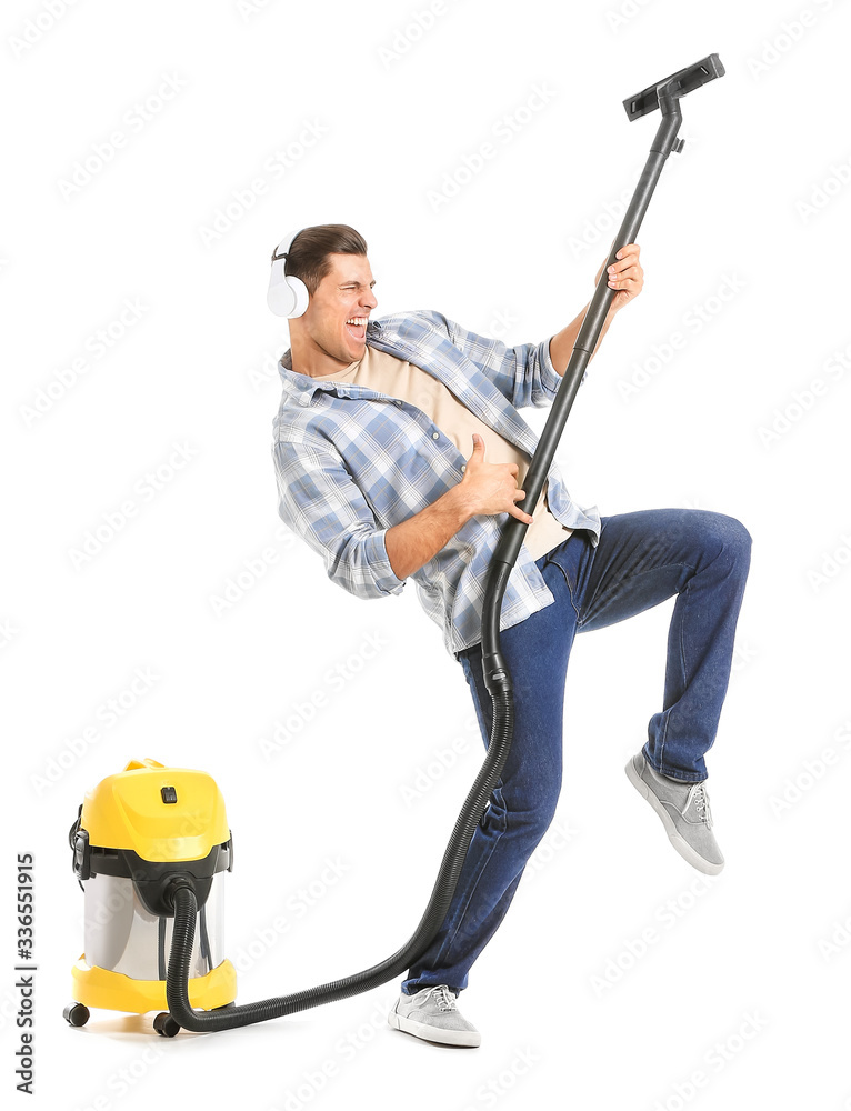 Young man with vacuum cleaner listening to music on white background