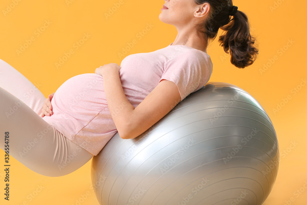 Young pregnant woman doing exercises with fitball on color background