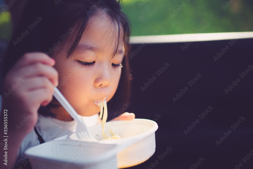 亚洲小女孩喜欢在车里用盒装意大利肉酱面和奶酪一起吃。