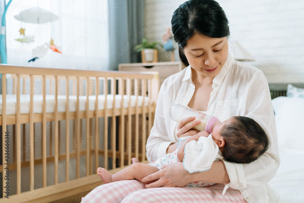 portrait asian lady lowering her head is sitting in bedroom feeding her baby. chinese mom looking he