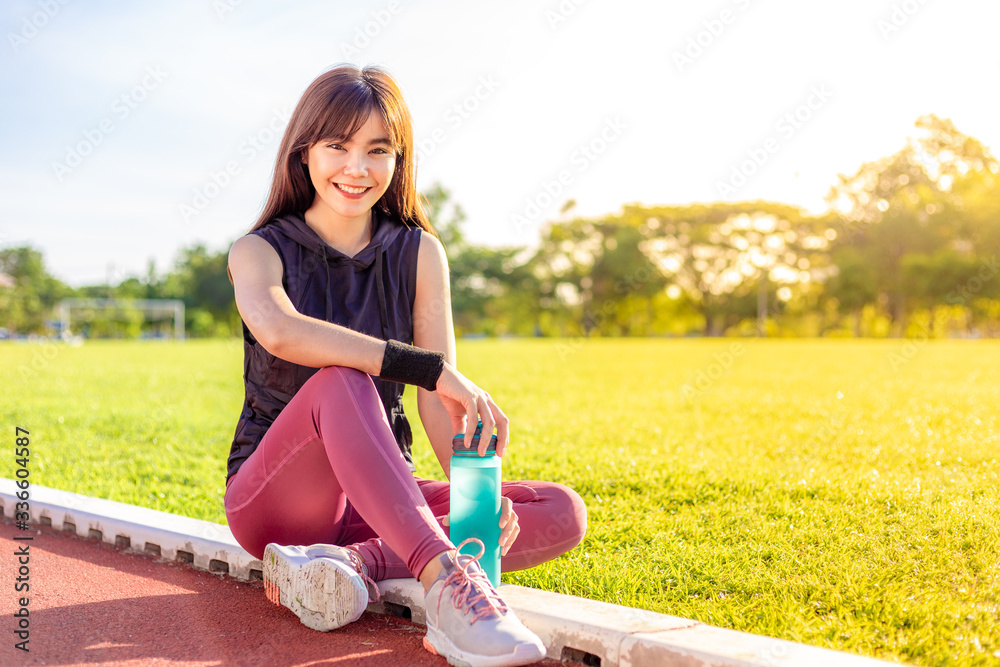 Happy beautiful young Asian woman stop to take a rest during her morning excercise at a running trac