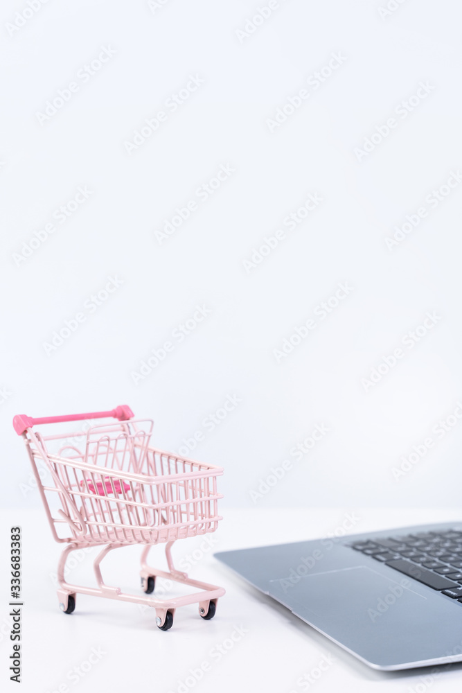 Online shopping. Mini empty pink shop cart trolley over a laptop computer on white table background,