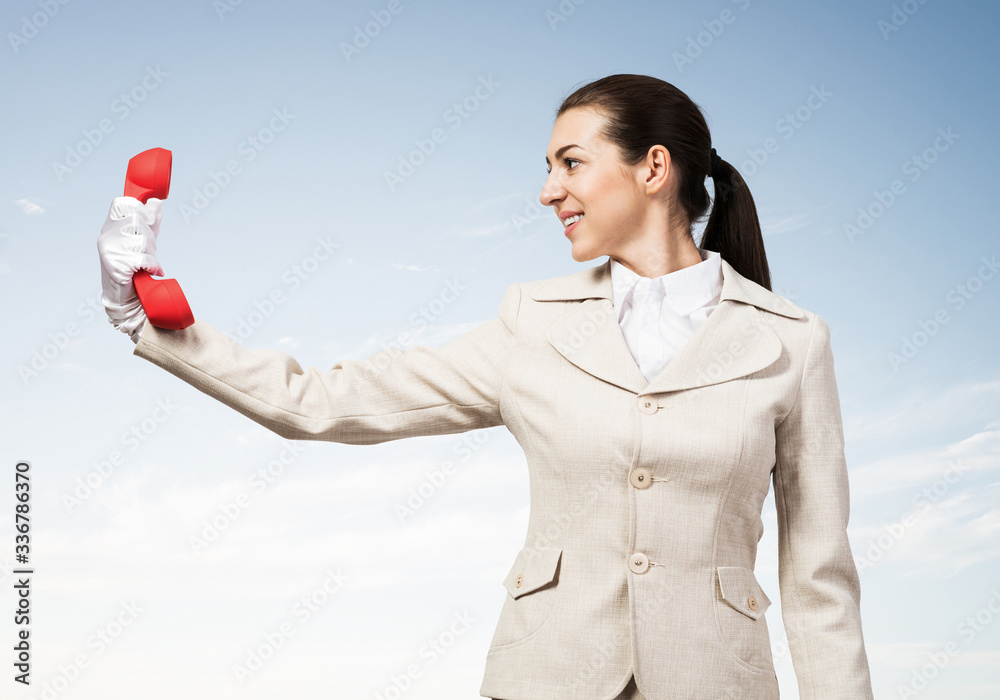 Smiling woman holds red handset phone on distance