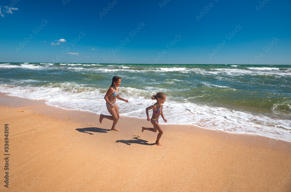 Two positive little girls run along the sandy beach on a sunny warm summer day. The concept of activ