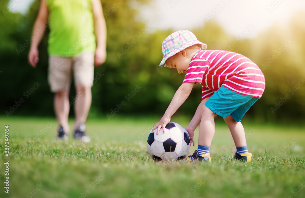 Little boy playting football on the field with gates