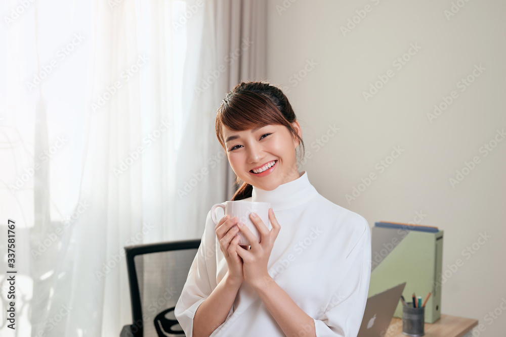 Portrait of cheerful Asian woman holding a cup of tea at her office