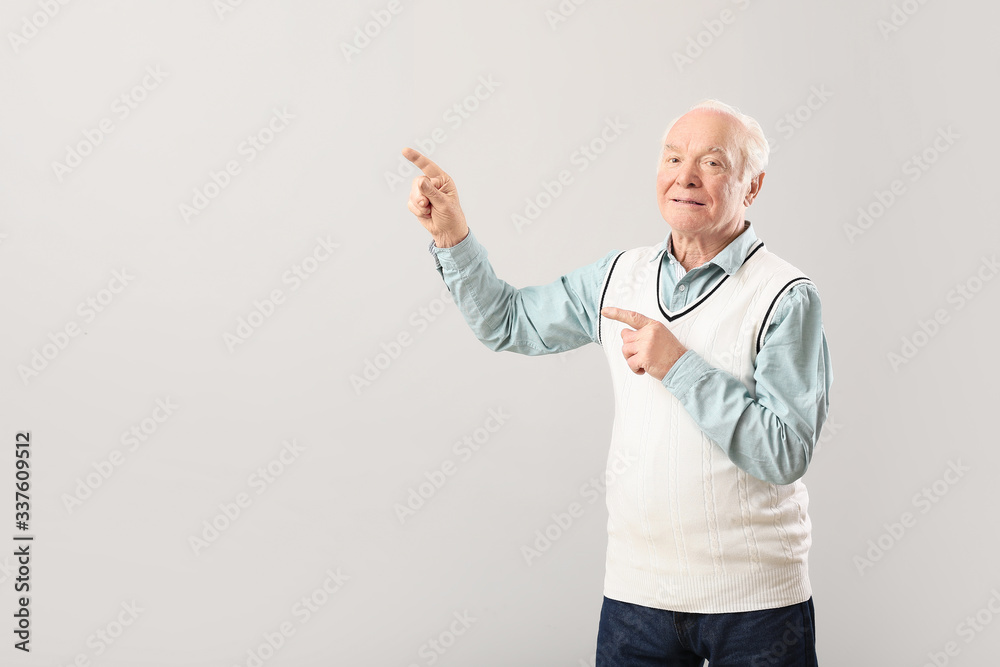 Portrait of elderly man showing something on grey background