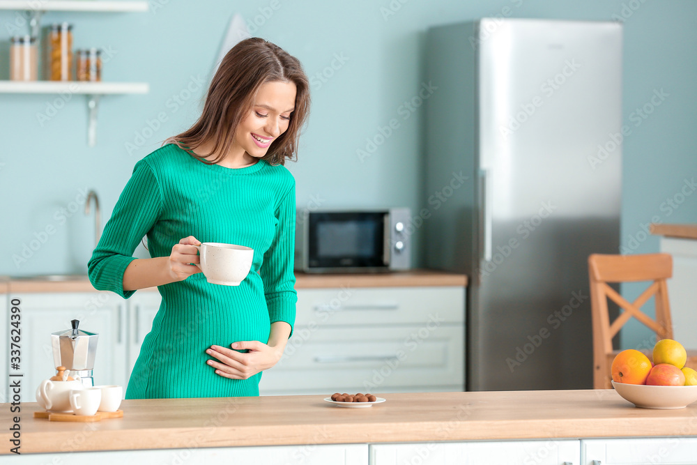 Beautiful pregnant woman with chocolate and tea in kitchen