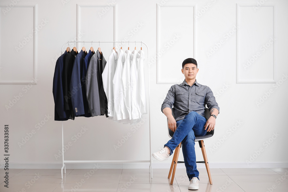 Male Asian stylist near rack with clothes in studio