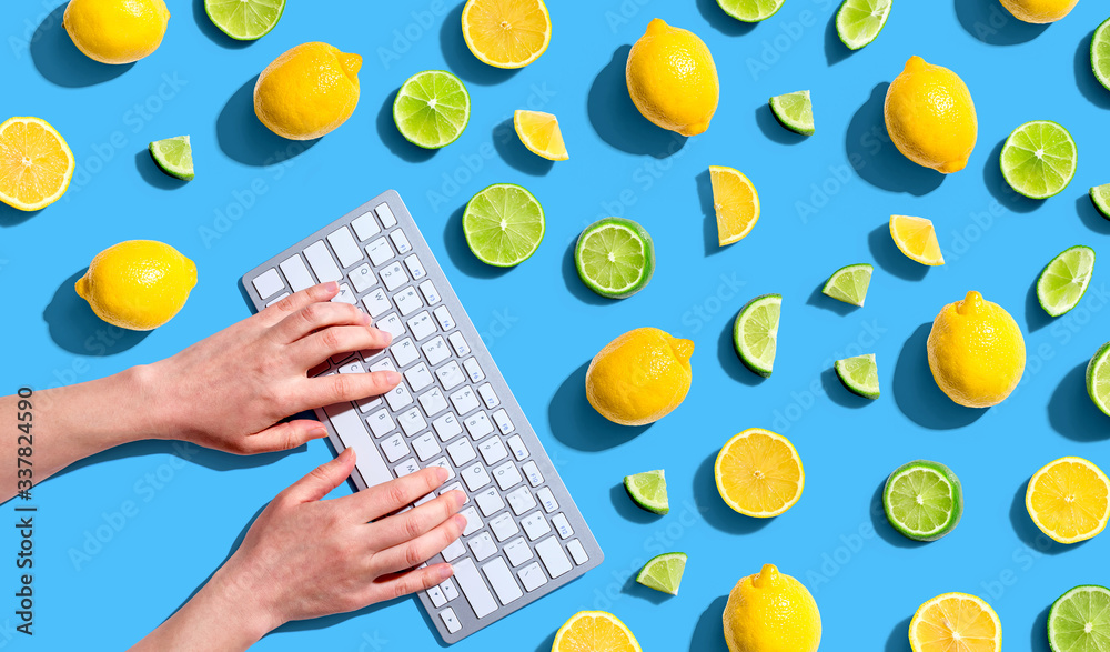 Woman using a computer keyboard with fresh lemons and limes overhead view - flat lay