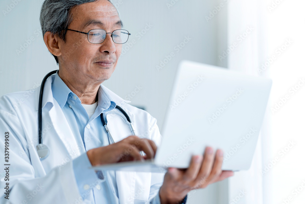 Senior asian male Doctor in hospital writing medical documentation and using laptop for manage white