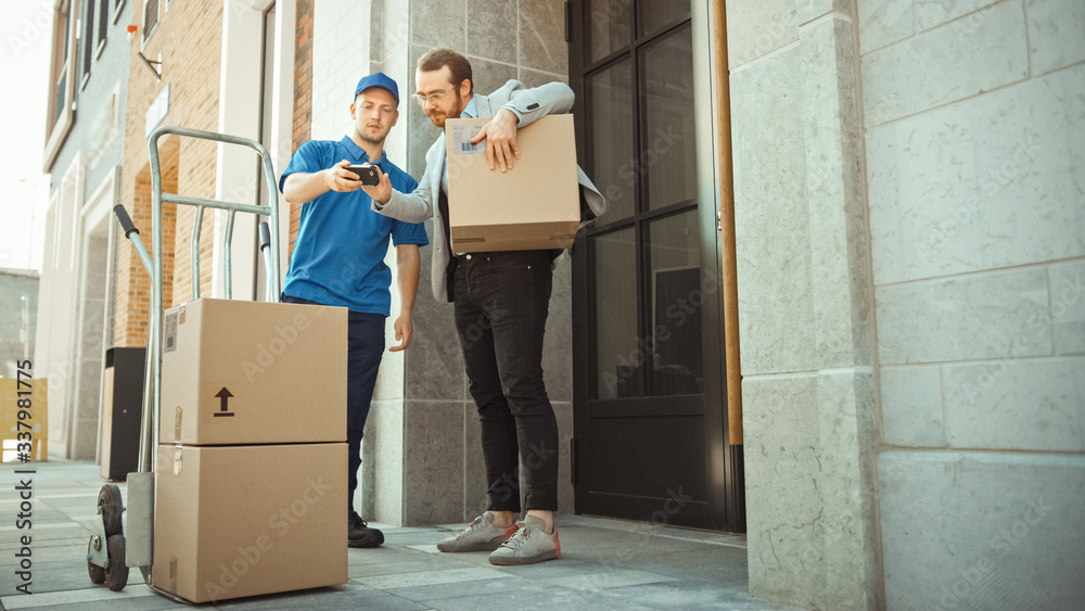 Delivery Man Pushes Hand Truck Trolley Full of Cardboard Boxes Hands Package to a Customer, Who then