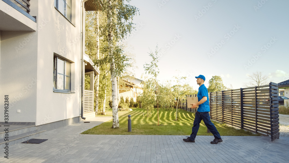 Delivery Man Holding Card Board Package Enters Through the Gates and Walks to the House. Delivering 