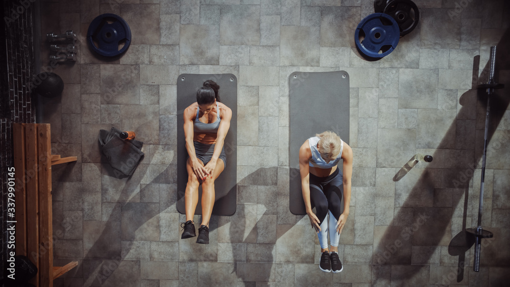 Two Professional Female Bodybuilders Doing Sit-up Exercises while Lying on the Yoga Mats in Hardcore