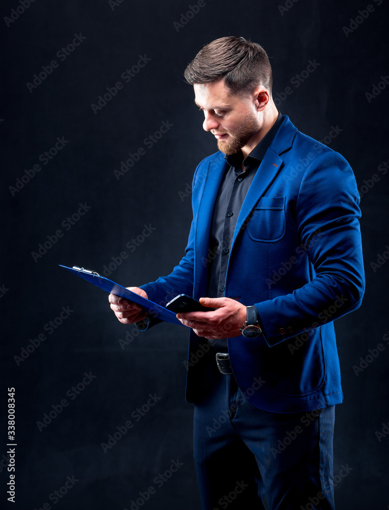 Portrait of handsome young successful man wearing dark shirt and blue suit holding blue folder, look