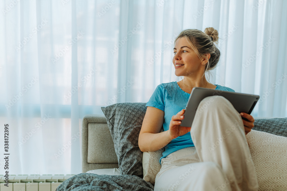 Portrait of smiling young woman in pajamas looking aside while sitting on bed and using tablet compu