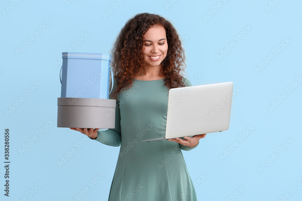 Young woman with laptop and boxes on color background. Online shopping concept