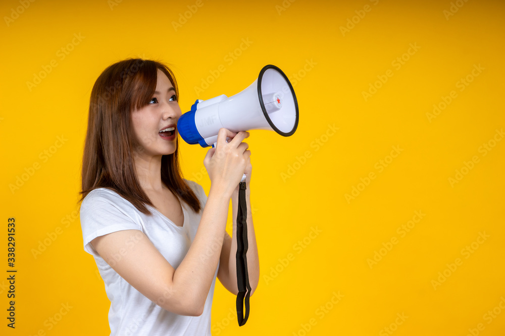 Young Asian woman in white casual t-shirt looking aside, scream in megaphone isolated on bright yell