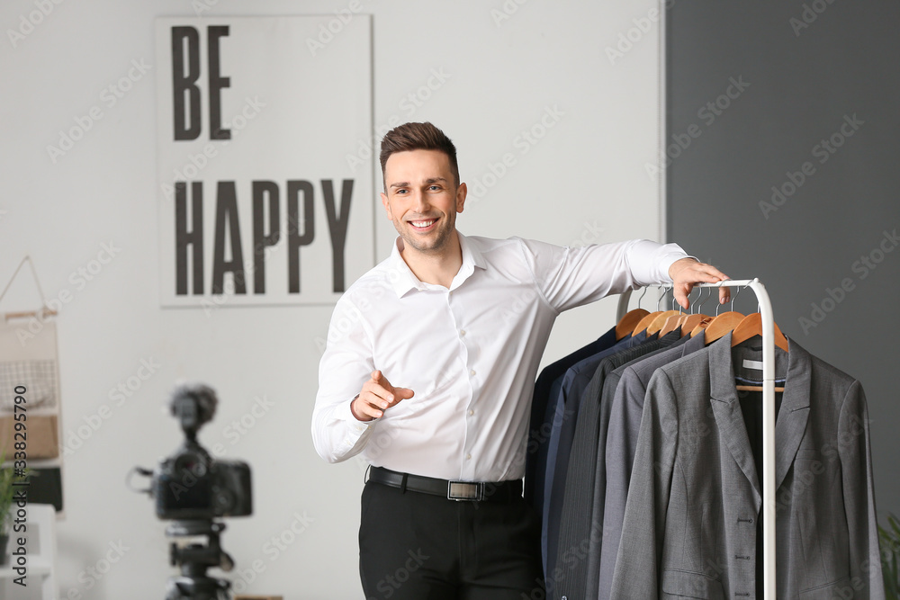 Young male stylist near rack with clothes in studio