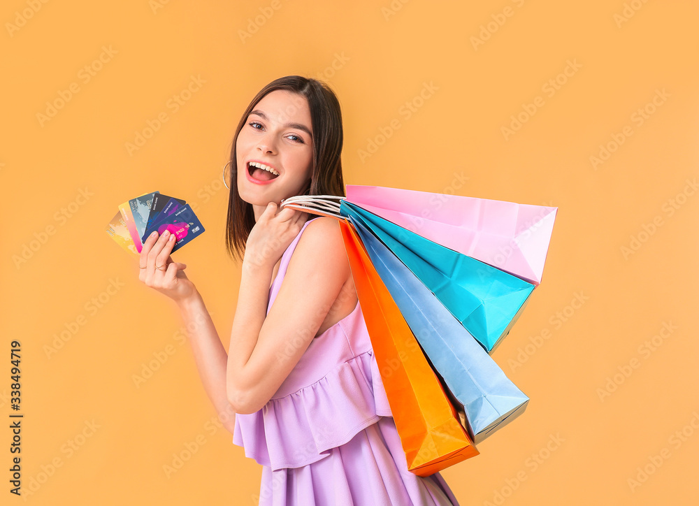 Beautiful young woman with shopping bags and credit cards on color background