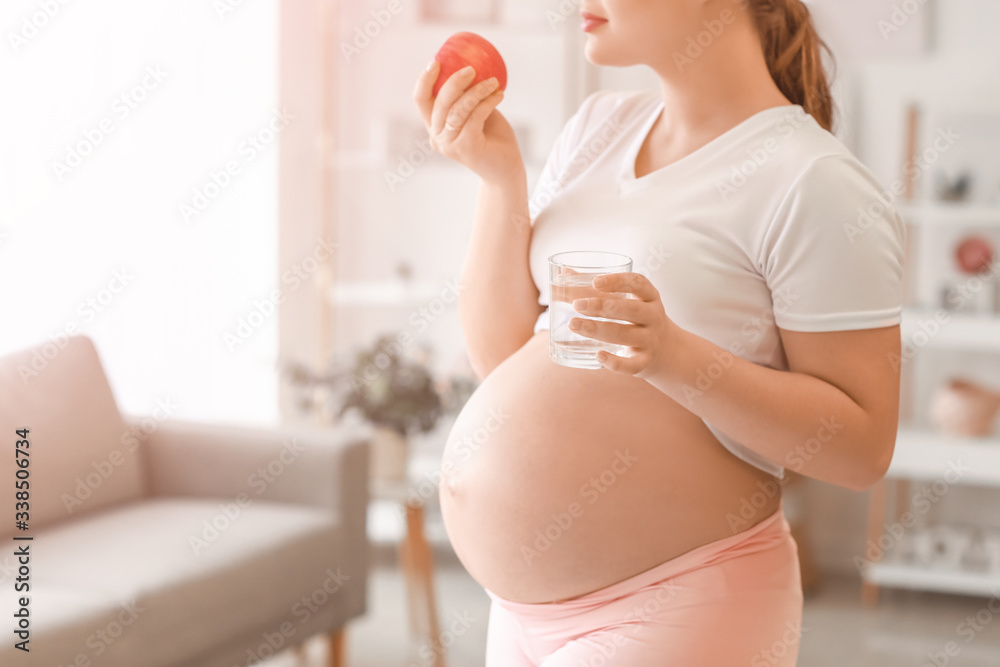 Beautiful pregnant woman with water and apple at home