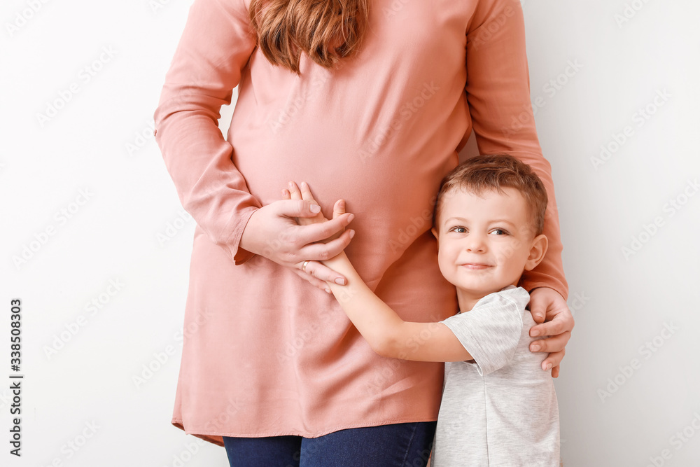 Beautiful pregnant woman with her little son on light background