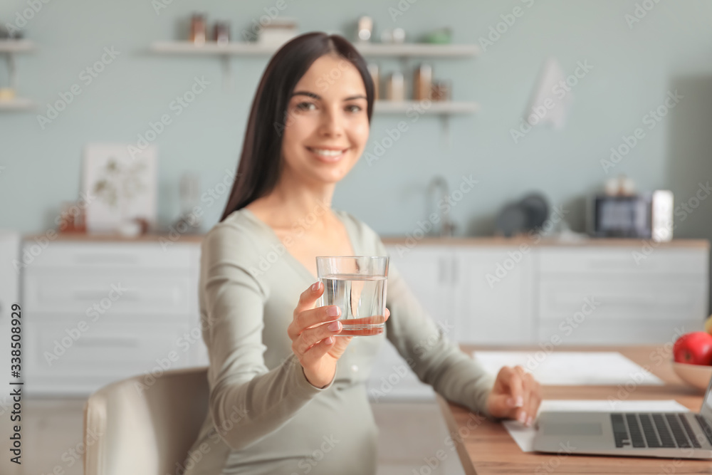 Beautiful pregnant woman drinking water in kitchen