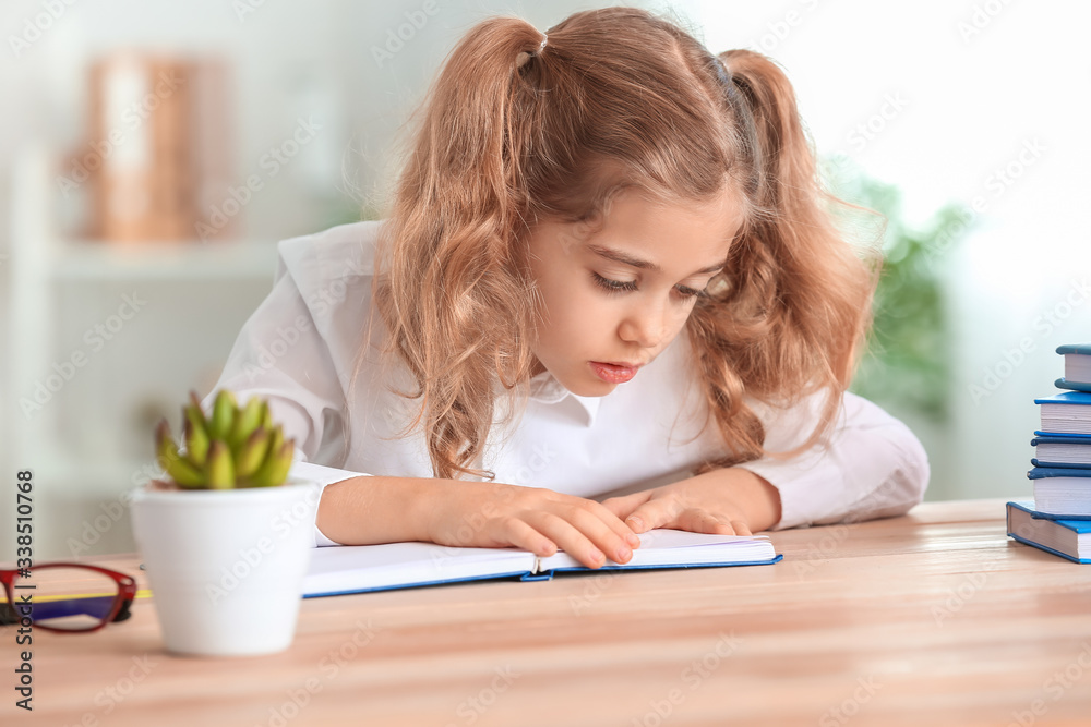 Cute little schoolgirl doing task at desk in classroom