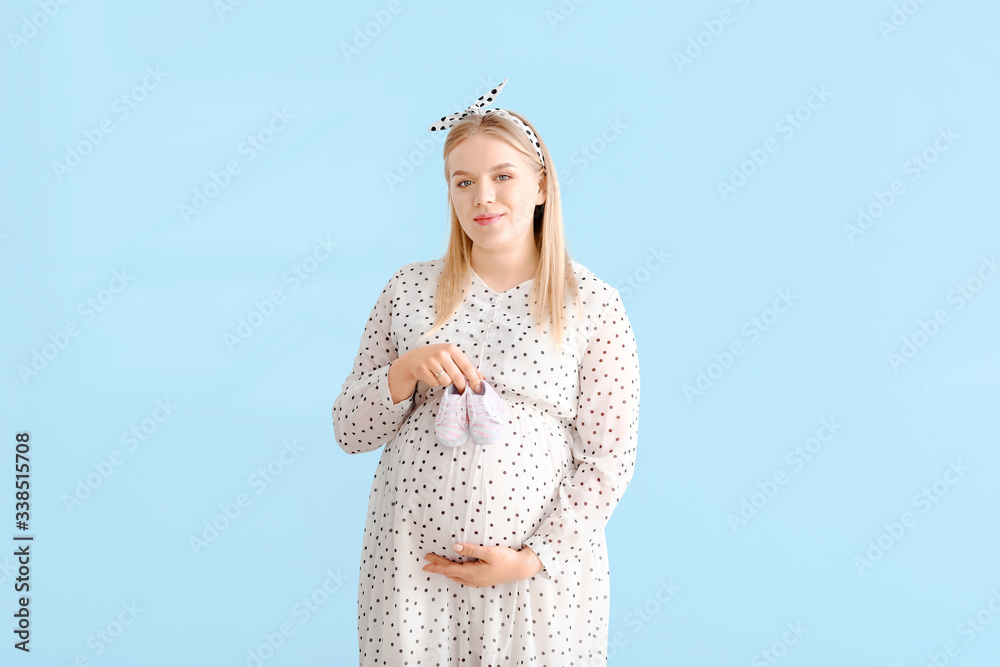 Beautiful pregnant woman with baby shoes on color background