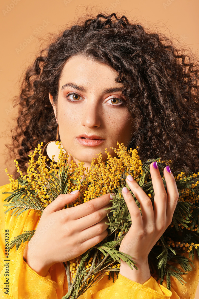 Young woman with beautiful curly hair and flowers on color background