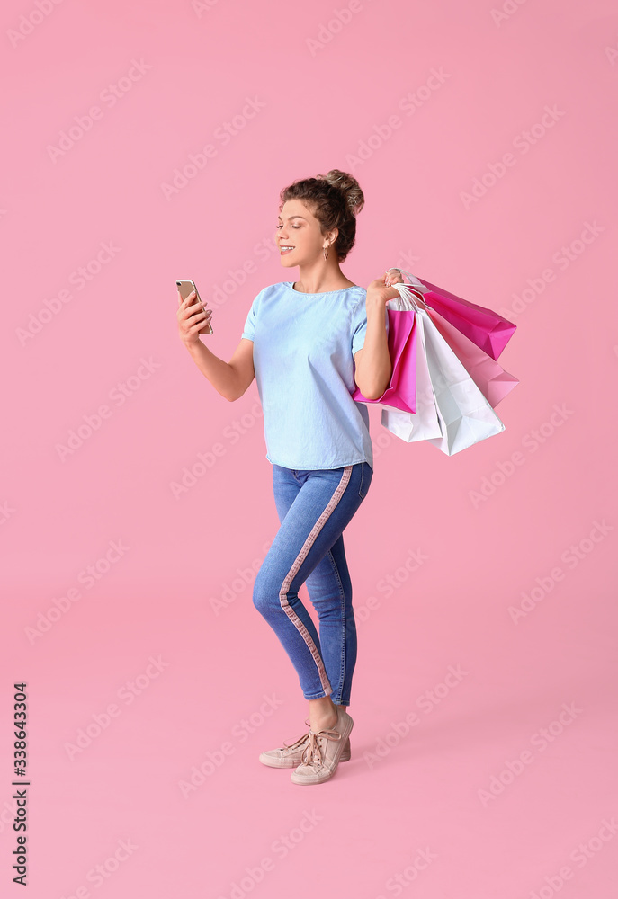 Beautiful young woman with mobile phone and shopping bags on color background